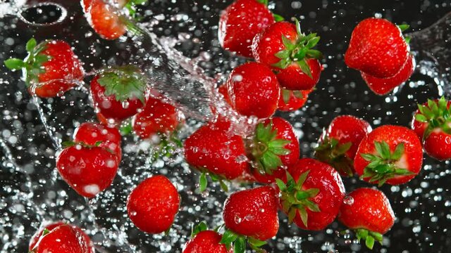 Super Slow Motion Shot of Flying Fresh Strawberries and Water Side Splash Isolated on Black at 1000 fps.