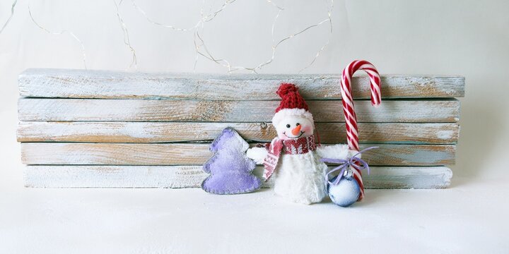 Toy snowman, caramel stick, Christmas decorations on a light wooden background, concept of congratulations, postcards