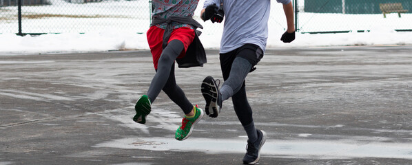Two runners bounding in a wet and icy parking lot after a snow storm