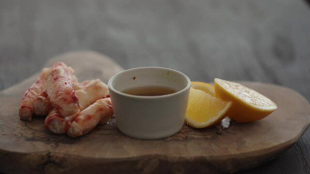 Slow motion gimbal shot of crab leg meat on a olive board with sweet lemon and dip sauce