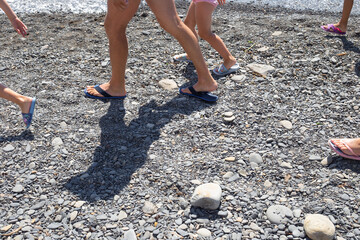 Legs of tourists walking along the pebbly seashore in summer. Travel and tourism