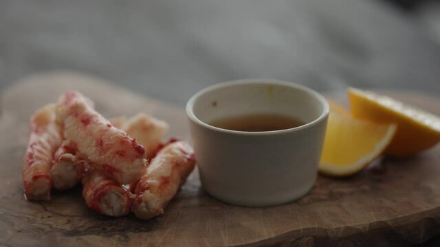 Slow motion gimbal shot of crab leg meat on a olive board with sweet lemon and dip sauce