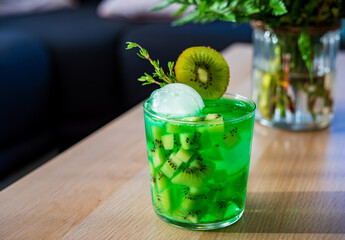 A glass of green Sweet cocktail kiwi mojito garnished with thyme and kiwi slice on wooden table in...