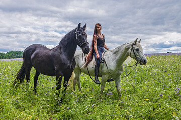 a young woman with long flowing hair rides a white horse and a Friesian pony runs with her