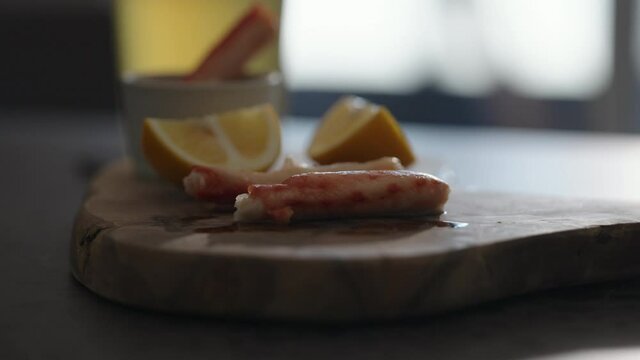 Slow motion gimbal shot of crab leg meat on a olive board with sweet lemon and dip sauce on concrete countertop