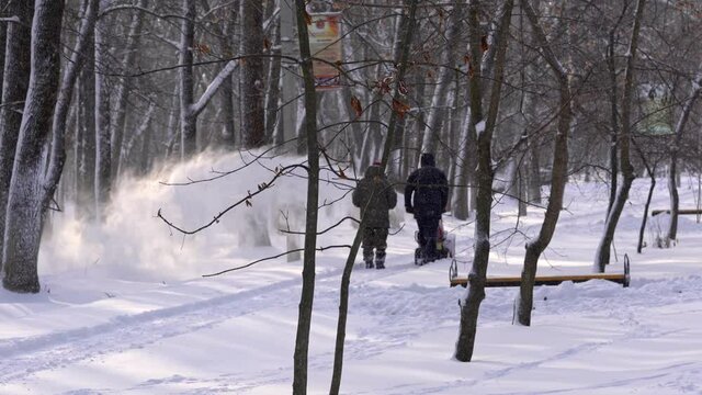 Men remove snow in the park with a snow blower