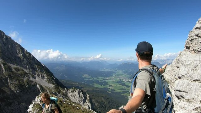 A couple standing on top of Grimming, highest self-standing mountain in Alps. They are dancing with happiness. High mountains around. Small village in the valley. Achievement and completion
