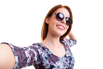 Beautiful smiling young girl with sunglasses taking a selfie, looking at the camera POV, isolated on white background. Attractive redhead girl with long hair taking a selfie.