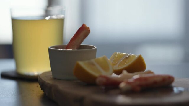 Slow motion gimbal shot of crab leg meat on a olive board with sweet lemon and dip sauce on concrete countertop