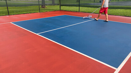 A pickleball court is dried using a squeegee