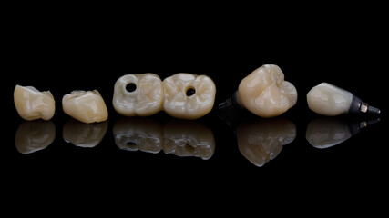 composition of beautiful dental ceramic crowns and inlays on black glass with reflection