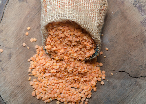 Heap of dry red lentils in Sack on wood background. Natural organic lentils. Dry uncooked red lentils grains.  
