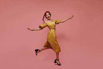 Emotional modern woman in red bandana, midi yellow dress and black shoes looking into camera and running on isolated background.. - Powered by Adobe