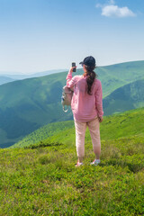 A tourist is relaxing in nature and uses the Internet on a smartphone. The girl traveler photographs a panorama of the mountains on a mobile phone. Mountain beautiful landscape