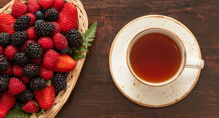 Berry tea. A cup of tea and berries in a basket on a wooden background. Banner. View from above.
