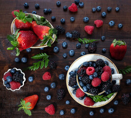 Berry mix on a wooden background. Berries in a cup and bowl. Strawberries, blueberries, blackberries and raspberries. Top view, flat lay.