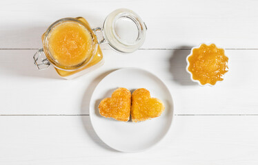 Fruit yellow jam on a white wooden background. Heart shaped delicious toast on a plate. Top view, flat lay.