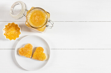 Fresh fruit jam on a white wooden background. Toast hearts in a plate. Yellow confiture. Copy space, top view, flat lay.