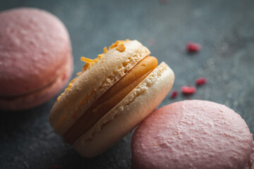 Flat lay of yellow and pink macaroons on the dark concrete background. Macro shot of cracked French sweet dessert cookies with crumbs