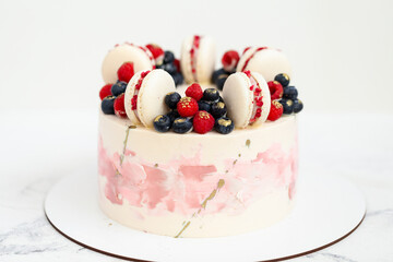 Birthday or anniversary cake with cream cheese frosting decorated with macaroons, blueberries and raspberries. Gold splash on the wedding cake. White background