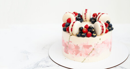 Birthday or anniversary cake with cream cheese frosting decorated with macaroons, blueberries and raspberries. Gold splash on the wedding cake. White background