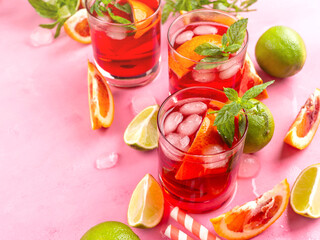 Refreshing summer red cocktail in glasses with blood orange and lime on pink background with mint