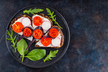 Healthy toasts with cream cheese, cherry tomatoes and spinach on black plate. Bruschetta with cream cheese and fresh herbs on a dark background. Copy space. Top view
