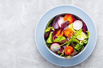 Healthy vegetable salad with cherry tomatoes, radish and mix salad. Vegan salad with mix of greens on gray background. Paleo diet concept. Copy space. Top view