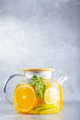 Detox lemonade drink of water, lemon, orange and mint leaves in a transparent teapot. Lime mint iced tea cocktail. Summer fresh drink. Copy space
