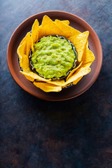 Traditional mexican sauce guacamole with tortilla chips in clay bowl. Bowl of guacamole with nachos chips on a dark background. Copy space. Top view
