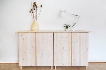 Light wooden sideboard with lamp and plant decoration against a white wall, minimal interior and home concept with copy space