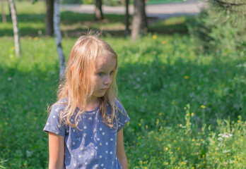 Obraz premium little girl, blonde six years old, with a displeased face, against the background of nature, portrait of a preschooler, with surprised eyes