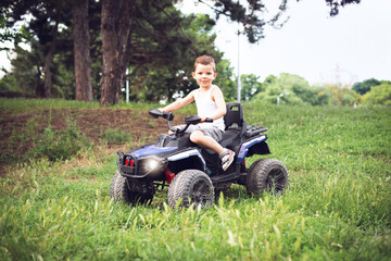 A cute five year old boy rides a black and purple ATV Quad bike in a summer park.