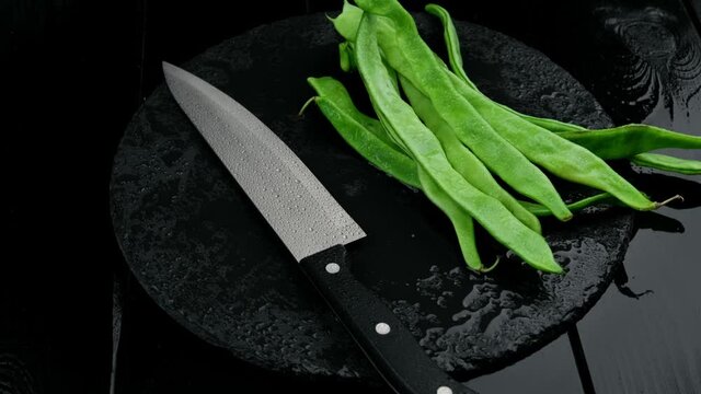 Fresh cut green beans and a knife on a rustic black wooden table.