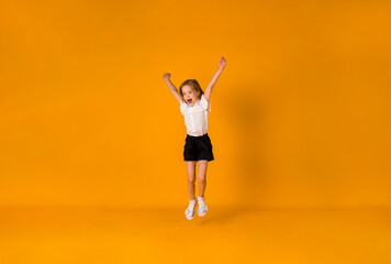 Fototapeta na wymiar happy blonde schoolgirl in uniform jumps on a yellow background with a copy of the space