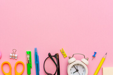 School supplies on a pink background. Back to school creative illustration, template. White alarm clock, black glasses and colorful accessories of bright color