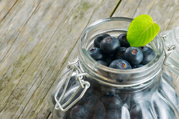 Jar full of Blueberries with a mint leaf over a old wooden table with negative space