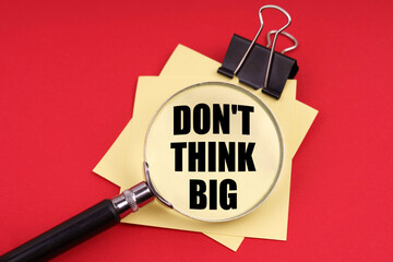 On a red background, a magnifying glass and a sticker with the inscription - Don t think big