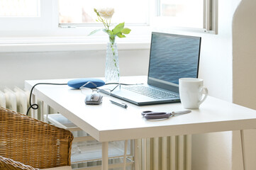 Small white desk at the window with a laptop as a workspace for studying or home office work, copy space