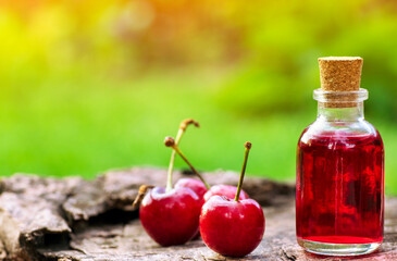 Cherries essence oil in a little bottle over a wood stump with cherries beside and green blurred background