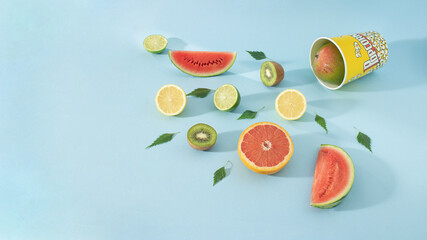 Creative cinema concept of spilled tropical fresh fruit from popcorn bucket. Summer organic food on pastel blue background.