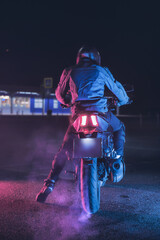 Motorcyclist makes a burnout on a motorbike in neon light, at night with clouds of tire smoke - 445795146