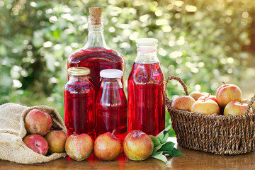 Bottles with Plums juice over awooden table with a basket and a bag with red Plums