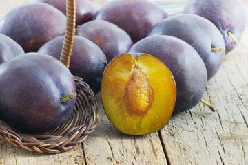Plums (Prunus Domestica) variety "President" over a wooden table with bright ambient and copy space. One plum is sliced cut in half and other is in a basket.