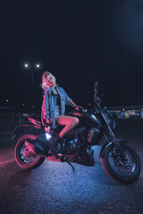 Naklejka na ściany i meble portrait of a girl in the rays of neon light on a motorbike at night in an empty parking lot