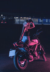 Fototapeta na wymiar portrait of a girl in the rays of neon light on a motorbike at night in an empty parking lot