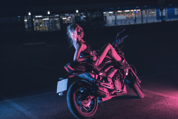 portrait of a girl in the rays of neon light on a motorbike at night in an empty parking lot - 445796546