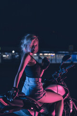 Naklejka na ściany i meble portrait of a girl in the rays of neon light on a motorbike at night in an empty parking lot