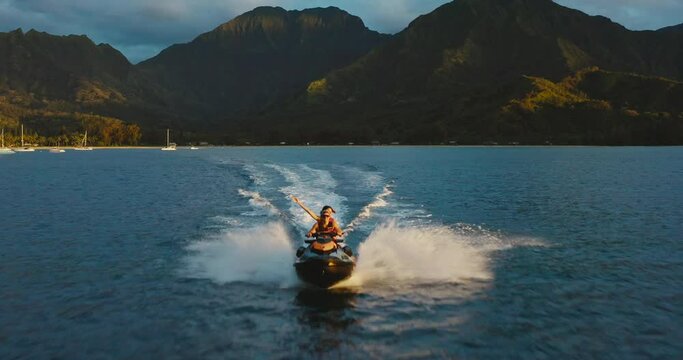Adventurous young couple riding jet ski in the ocean at sunset, stunning tropical mountains, epic vacation lifestyle