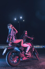 Naklejka na ściany i meble a couple of girls in love on a motorbike in the rays of neon light in an empty parking lot at night